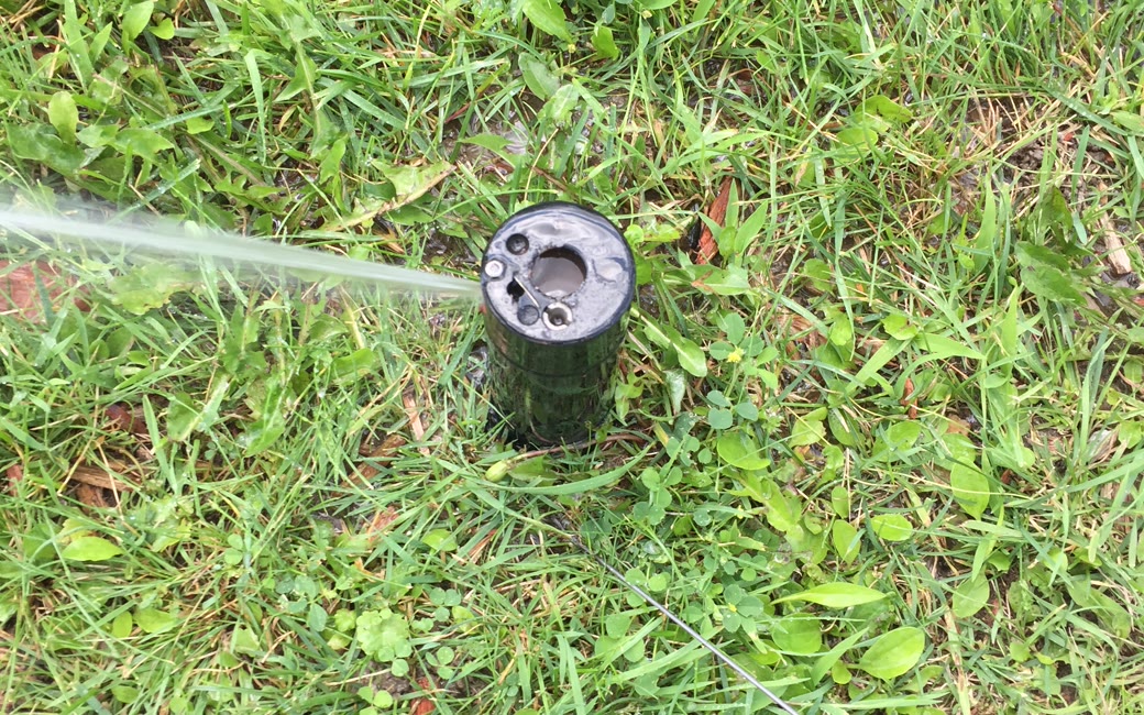 A sprinkler head with a missing nozzle spraying sideways instead of misting