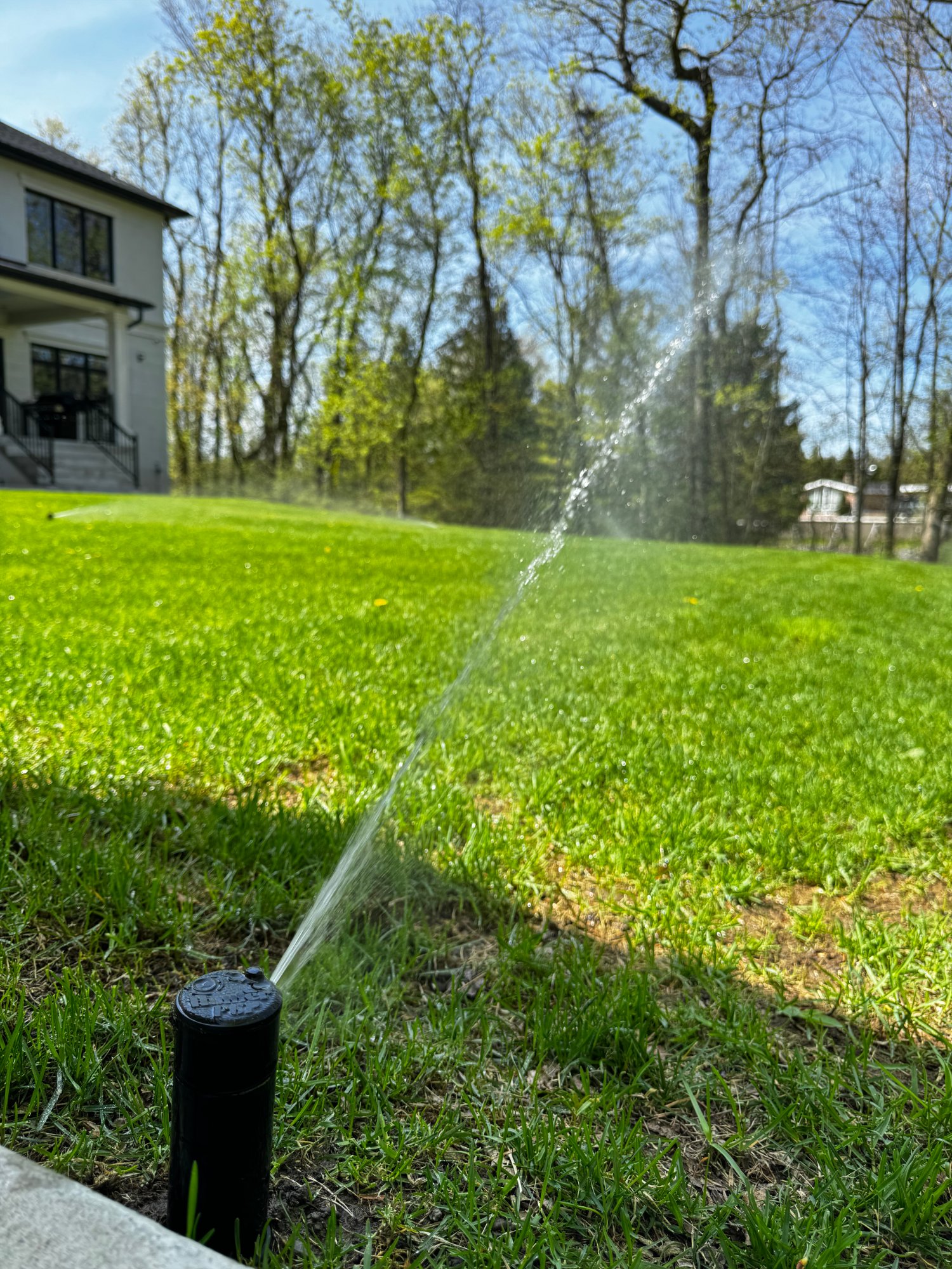 A pop-up rotor sprinkler running on a healthy green lawn in front of a GTA home