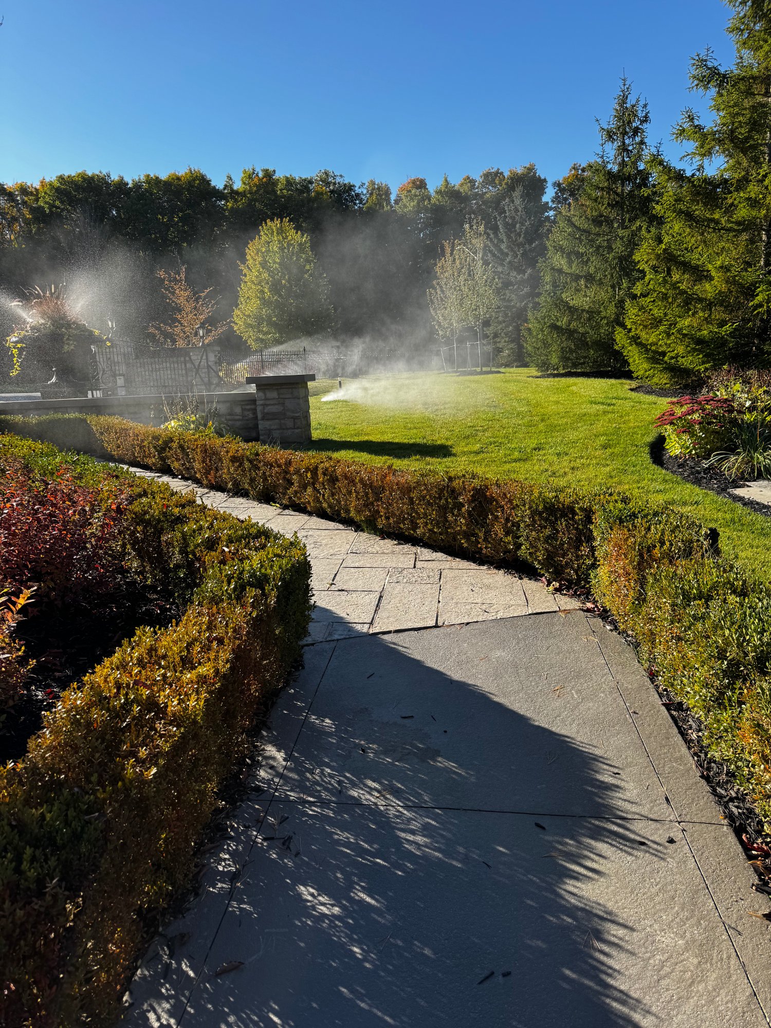 An irrigation system running across a landscaped estate lawn and garden beds