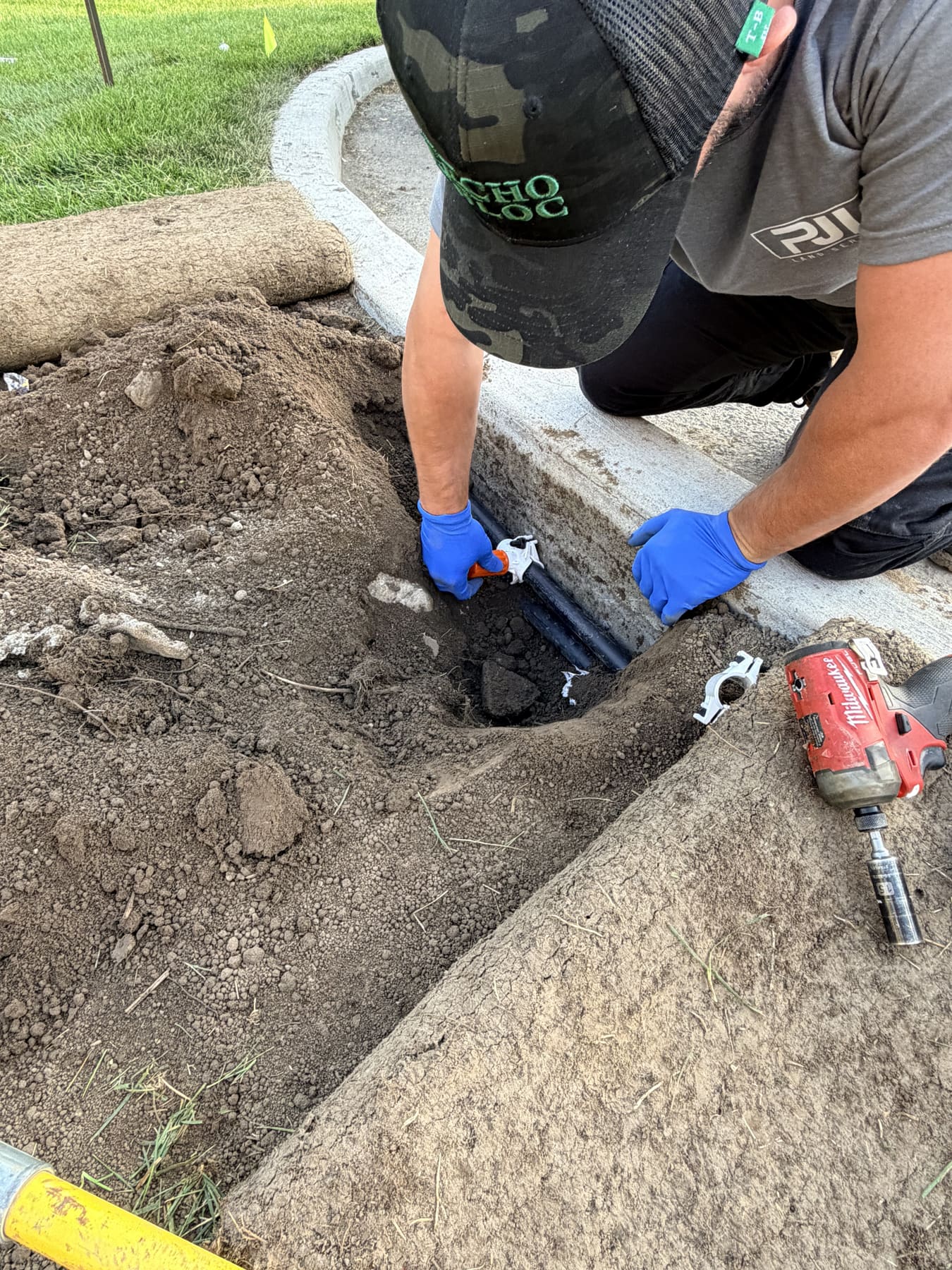 Close-up of a PJL Land Services technician in nitrile gloves fitting an irrigation mainline coupling in a dirt trench